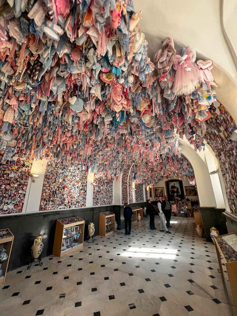 Sala con la volta coperta di fiocchi rosa e azzurri e le pareti di fotografie; alcuni visitatori in fondo.